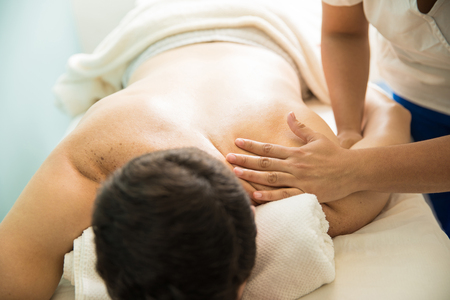 Closeup of the hands of a female therapist giving a back massage to a young man in a health spaの写真素材