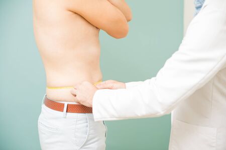 Closeup of a young man visiting his doctor and getting his waistline measuredの写真素材
