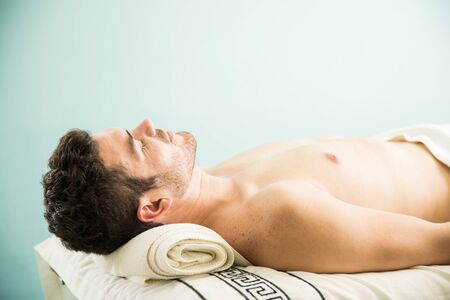 Profile view of a young man lying on a bed and taking a nap after a massage in a spaの写真素材