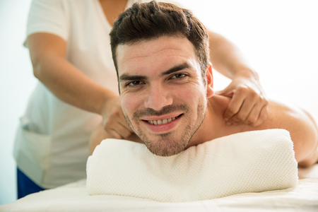 Portrait of a handsome Hispanic young man getting a back massage and smiling in a health spaの写真素材