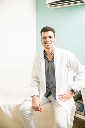 Good looking young Hispanic therapist sitting on a massage bed and ready to work in a health clinic and spaの写真素材