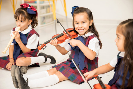 Portrait of a cute Latin girl learning how to play the violin and having fun in preschoolの写真素材