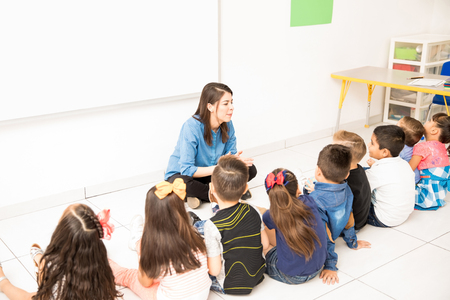 Group of preschool students and their teacher sitting in the classroom floor and learningの写真素材