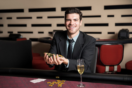 Happy young man sitting at a casino table with hand full of chips after winning a poker gameの写真素材