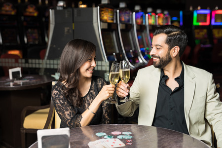 Latin couple making a toast with champagne while sitting in a casino restaurant on a dateの写真素材