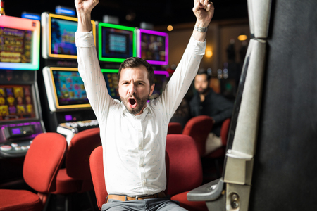 Portrait of an attractive Hispanic man looking very excited about winning some money playing slots in a casinoの写真素材
