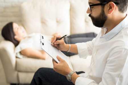 Psychologist making notes during a psychotherapy session with female patient  の写真素材