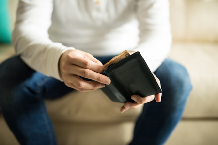 Close up of young man sitting on sofa taking out money from his wallet