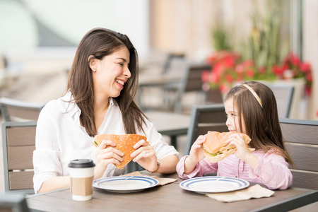 Pretty young hispanic mother and daughter eating a big burger at a cafe and smilingの写真素材
