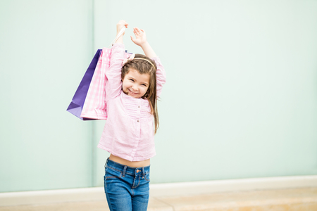 Portrait of beautiful little latin girl standing outside a store holding shopping bagsの写真素材