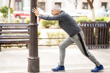 Full length of a hispanic mature man in his 50s doing stretching exercises before going for a run in the cityの写真素材