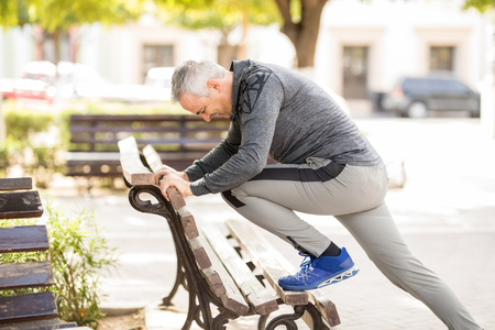 Hispanic middle aged man stretching on park benchの写真素材