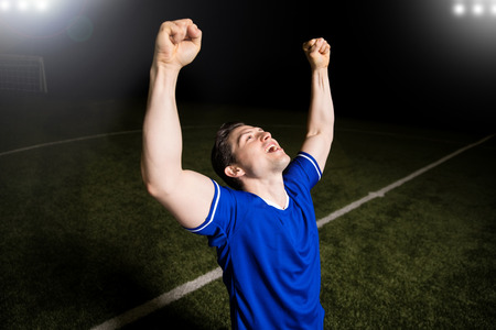 Cheerful male footballer raising his arms and celebrating his victory in the stadiumの写真素材