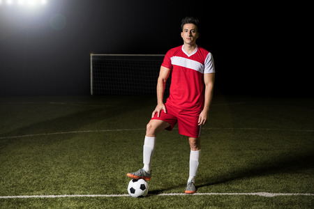 Full length of young football team player standing with his foot on the soccer ball outdoors on fieldの写真素材