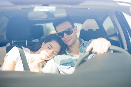 Portrait of a handsome young man driving a car while his girlfriend falls asleep on his shoulder