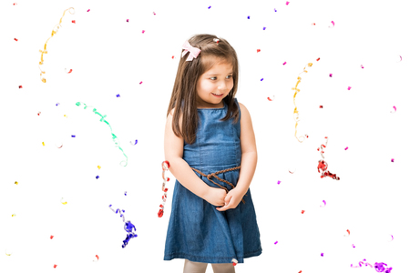 Portrait of beautiful little girl child standing on white background and smiling with confetti falling aroundの写真素材