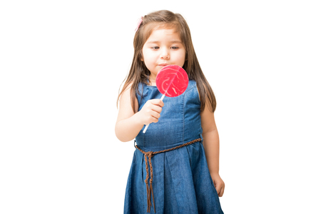 Portrait of beautiful little girl holding huge lollipop against white backgroundの写真素材