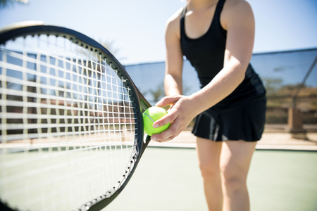 Close up of a young woman ready to hit a tennis ball, serving a ball during game.の写真素材
