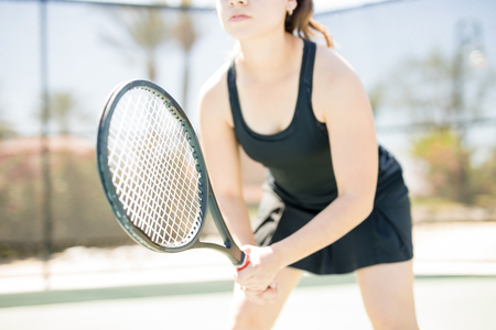Close up of racket in hands of female tennis player reading to face the serve on outdoors court during trainingの写真素材