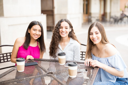 Portrait of beautiful young girl friends sitting at a cafe having coffeeの写真素材