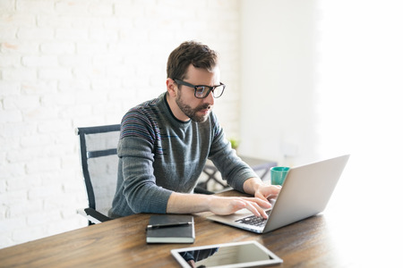 Handsome young latin man working on laptop while sitting at table in his office