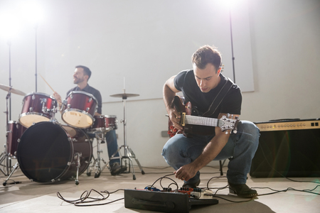 Young male guitarist setting up guitar audio processing effects on stageの写真素材