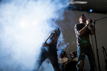 Rock singer performing on stage with guitarist. Bright light and smoke on stage.の写真素材