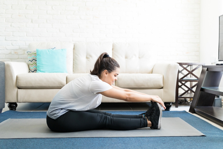 Side view of fit young woman doing stretching exercising sitting on yoga mat in living room