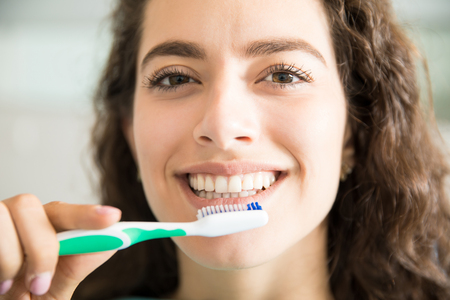Closeup portrait of beautiful young woman brushing teeth in dental clinicの写真素材