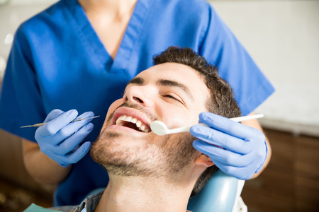 Mid adult patient receiving dental treatment with tools from female dentist in clinicの写真素材