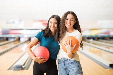 Smiling female friends with bowling balls hanging out in alley at clubの写真素材