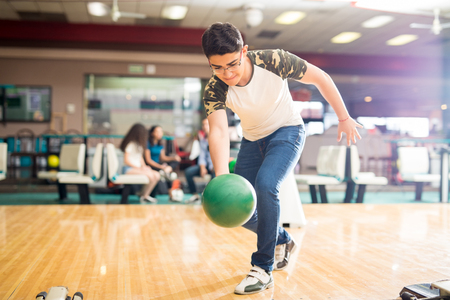 Full length of confident teenage boy practicing his swing at a bowling alleyの写真素材