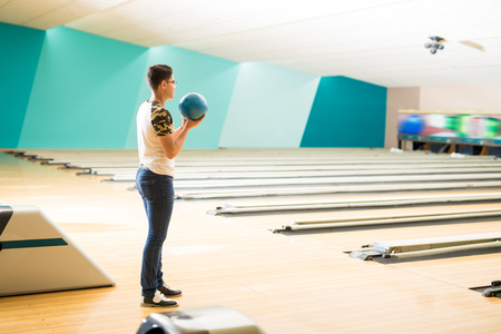 Full length side view of confident teen boy practicing bowling in clubの写真素材