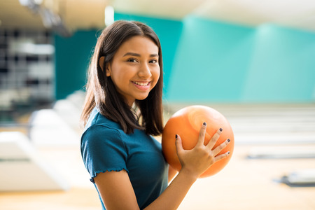 Smiling teenage girl with ball having fun at bowling alley in clubの写真素材