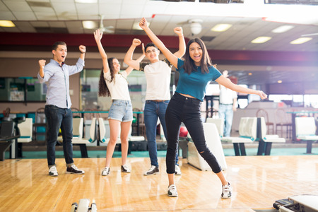 Happy multi-ethnic friends enjoying victory while standing at bowling clubの写真素材