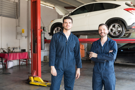 Portrait of colleagues wearing uniforms while standing together against car lift in garageの写真素材