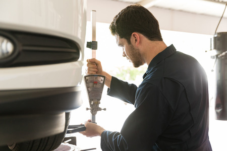 Car mechanic examining tire alignment with camber adapter in auto repair shopの写真素材