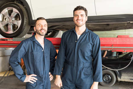 Portrait of confident male mechanics smiling in auto repair shopの写真素材
