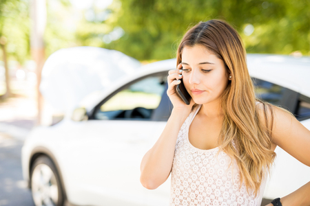 Pretty young woman calling for assistance with her car broken down by the roadsideの写真素材