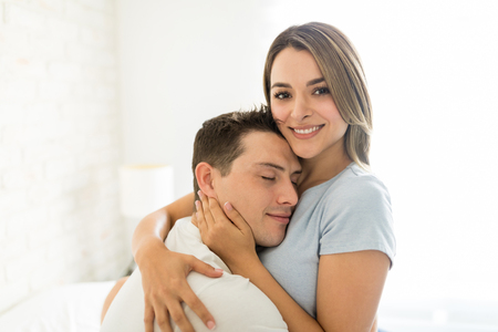 Pretty female smiling while embracing man with affection at homeの写真素材