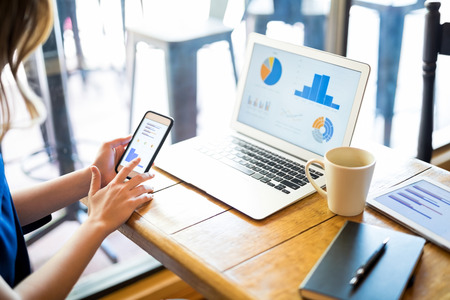 Close up of a woman sitting at table in coffee shop looking at chart on mobile screen and developing business planの写真素材