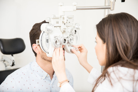 Beautiful woman optometrist performing eye checkup with phoropter at clinicの写真素材