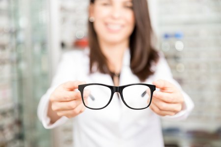 Smiling woman in blur background in optical store showing black classic frame for spectaclesの写真素材