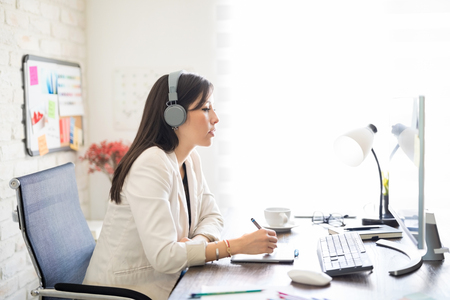 Side view of creative female designer wearing headphones making a design with drawing tablet and looking at computer screen.の写真素材