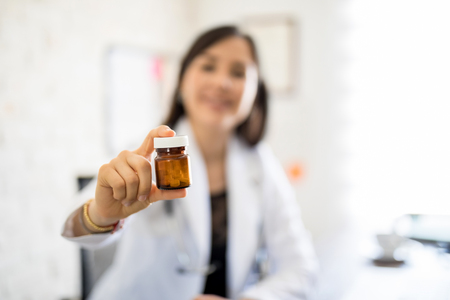 Female doctor holding out a bottle of pills at her clinicの写真素材