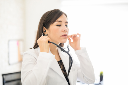 Portrait of latin female doctor using a stethoscope at clinicの写真素材