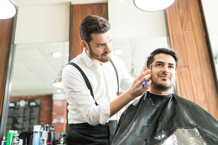Low angle view of confident male barber styling client's beard in shopの写真素材