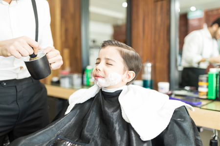 Midsection of barber applying shaving foam on boy's face in shopの写真素材