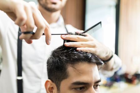 Hands of barber using scissors to cut customer's hair in salonの写真素材