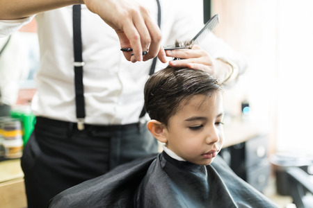 Closeup of boy having haircut with comb and scissors at barber shopの写真素材